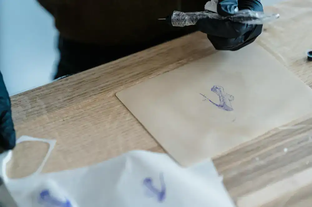 A tattoo machine resting on a workstation next to ink caps and stencil paper